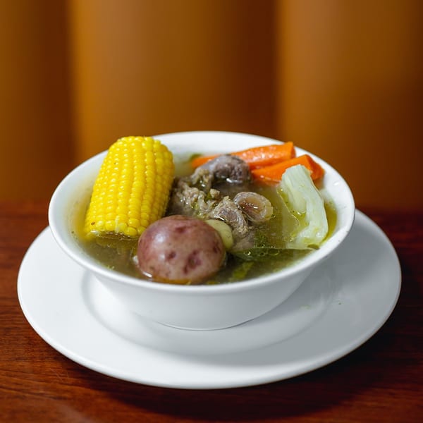 Hearty Mexican beef soup with corn on the cob, potatoes, carrots, and cabbage in a white bowl.