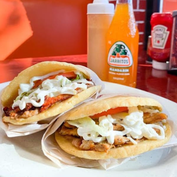 Two Mexican gorditas filled with meat, lettuce, tomato, and crema, with a Jarritos soda.