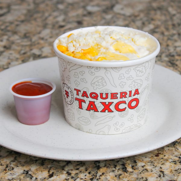 Taqueria Taxco branded cup of esquites with cheese and corn, next to a small cup of salsa.