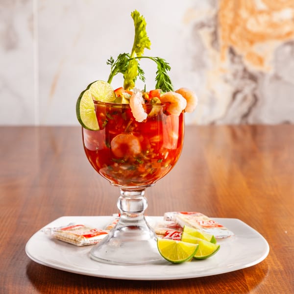 Shrimp cocktail in a goblet with lime, celery, and crackers on a white plate.