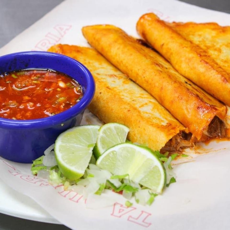 Taqueria Taxco's crispy taquitos with a side of red salsa, shredded lettuce, and lime wedges.