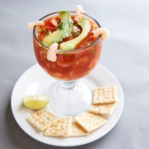 Shrimp cocktail with avocado slices and cilantro in a goblet, served with crackers and lime.
