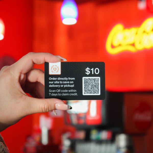 Hand holding a black $10 Taqueria Taxco gift card with a QR code against a red background.