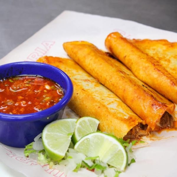 Taqueria Taxco's crispy taquitos with a side of red salsa, shredded lettuce, and lime wedges.