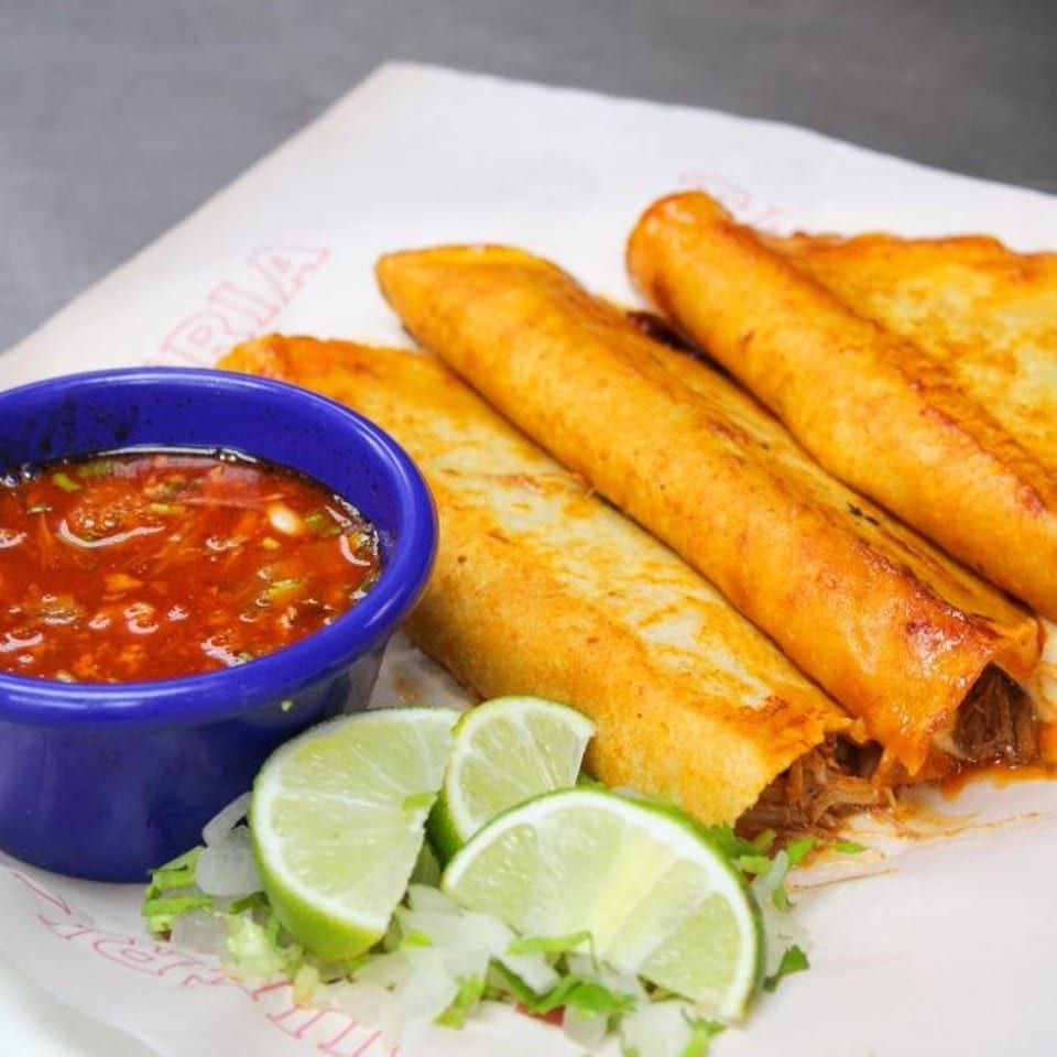 Taqueria Taxco's crispy flautas with a side of red salsa, shredded lettuce, and lime wedges.