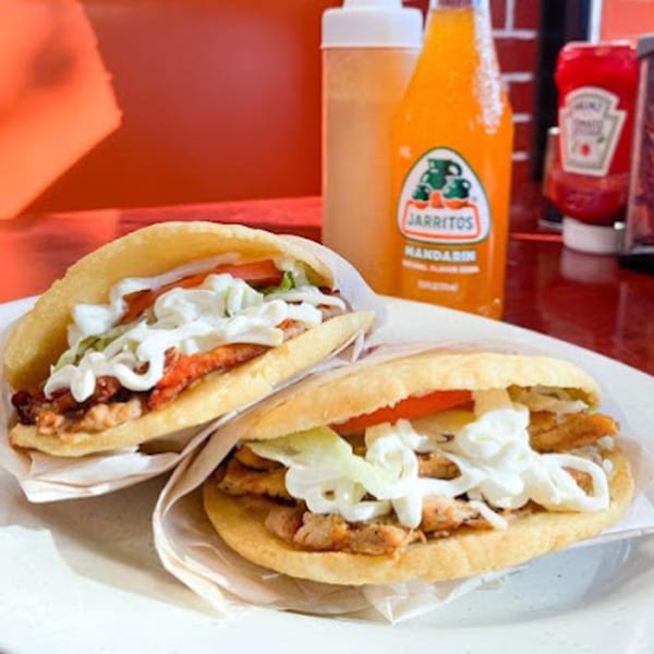 Two gorditas filled with meat, lettuce, tomato, and crema, with a Jarritos soda in the background.